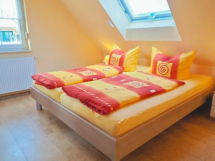 Blick ins kleinere Schlafzimmer. Das Dachflächenfenster ist mit einer Außenjalousie versehen.