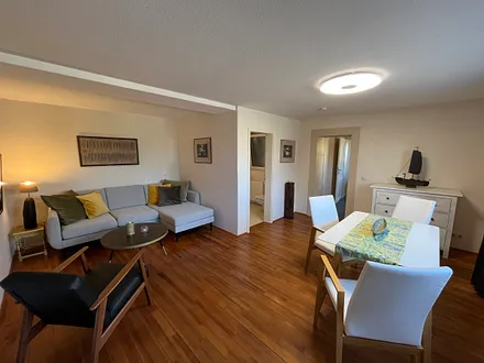 Großes Wohnzimmer mit bequemer Couch, Sessel und Essgruppe, Zugang zu Küche und Badezimmer