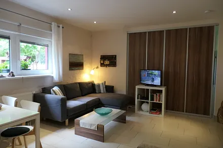 Modern eingerichteter Wohnraum mit Sitzecke, SAT-TV/Radio, im Hintergrund Schiebetür mit Durchgang zum Schlafzimmer