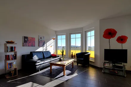 Wohnzimmerecke mit Schlafcouch, großen Erkerfenstern und Blick auf den Zickersee und den Greifswalder Bodden/Ostsee.