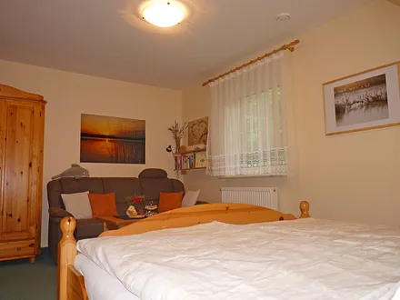 Wohnbereich mit Kleiderschrank, Sofa (ggf. ausklappbar zur Doppelbettcouch bei Aufbettung für max. 1 Pers.), kleinem Tisch und Sessel und Wandboard