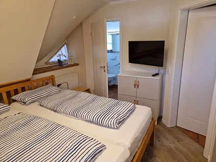Schlafzimmer 1 im 1. OG mit Doppelbett, angrenzendem Duschbad und TV