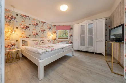 Schlafzimmer mit TV.  Das Doppelbett ist bequeme 1,80x2m breit. Plissee und Raffrollo am Fenster haben Verdunkelungsfunktion.