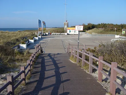 Strandpromenade und "Strandplateau" mit vielen Sitzbänken in der Sonne und Blick auf Strand und Ostsee. Im Hintergrund die DLRG-Wachstation.
