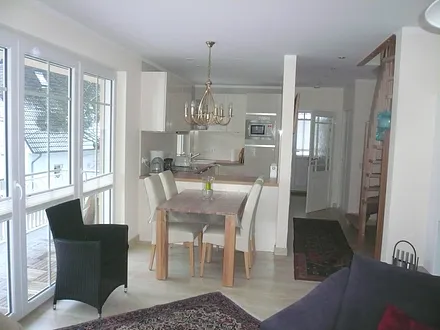 Essbereich mit dimmbarem Kronleuchter. 6 Stühle, im Hintergrund die offene Küche, rechts die Treppe in den Schlafbereich, links Zugang zum zusätzlichen Balkon,  Balkontür mit Fliegengitter