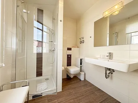 Badezimmer mit Dusche, WC, Waschbecken, Kosmetikspiegel, Handtuchwärmeheizkörper und Fön