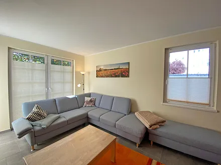 Wohnzimmer mit gemütlicher Eck- Couch mit Hocker, Couchtisch, Stehlampe, zwei Vitrinen, TV-Board mit Flachbild-TV sowie DVD-Player und CD-Player