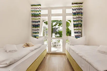 Im zweiten Schlafzimmer befinden sich zwei Boxspringbetten, die je nach Bedarf einzeln oder zusammen gestellt werden können. Kleiderschrank und Verdunkelungsgardinen sind ebenfalls vorhanden.