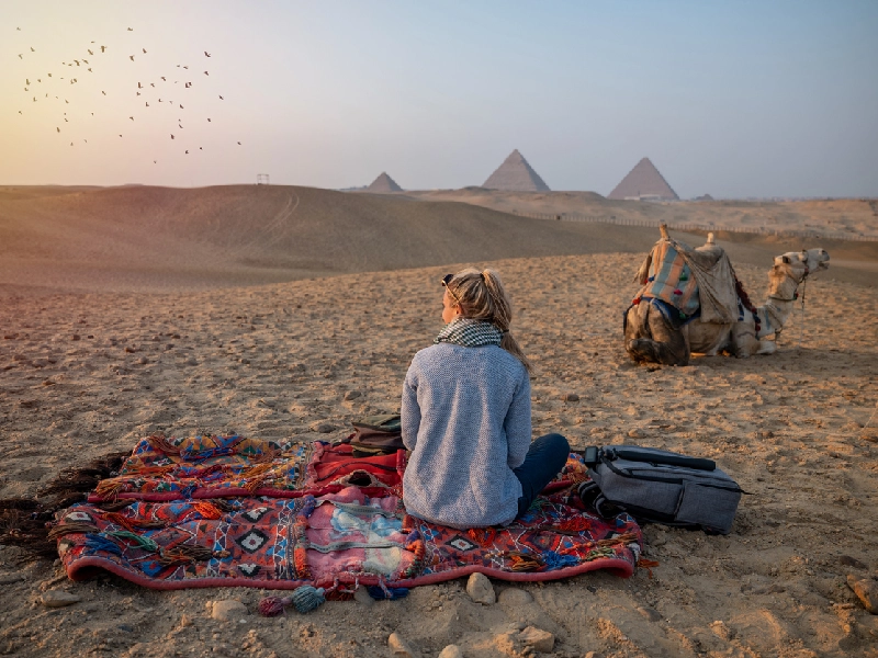 Una donna seduta vicino ad un cammello sulla sabbia delle Piramidi di Giza, il cairo cosa vedere