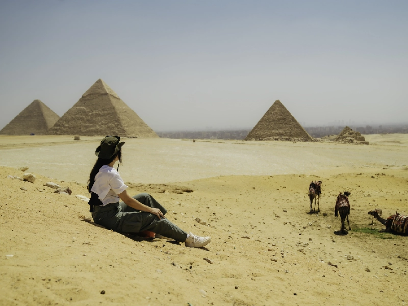 Una donna seduta sul deserto vicino alle Piramidi di Giza, il cairo cosa vedere
