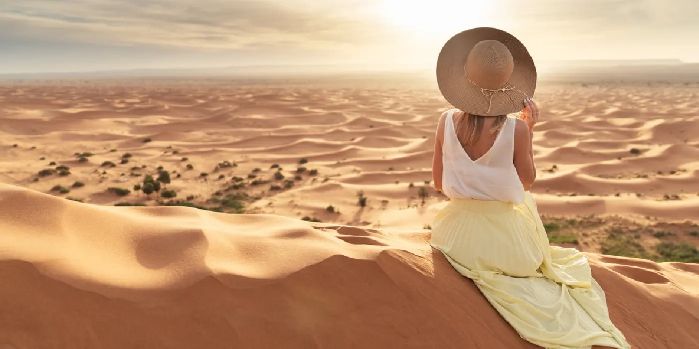 Woman in yellow skirt watches sunrise over Merzouga dunes.