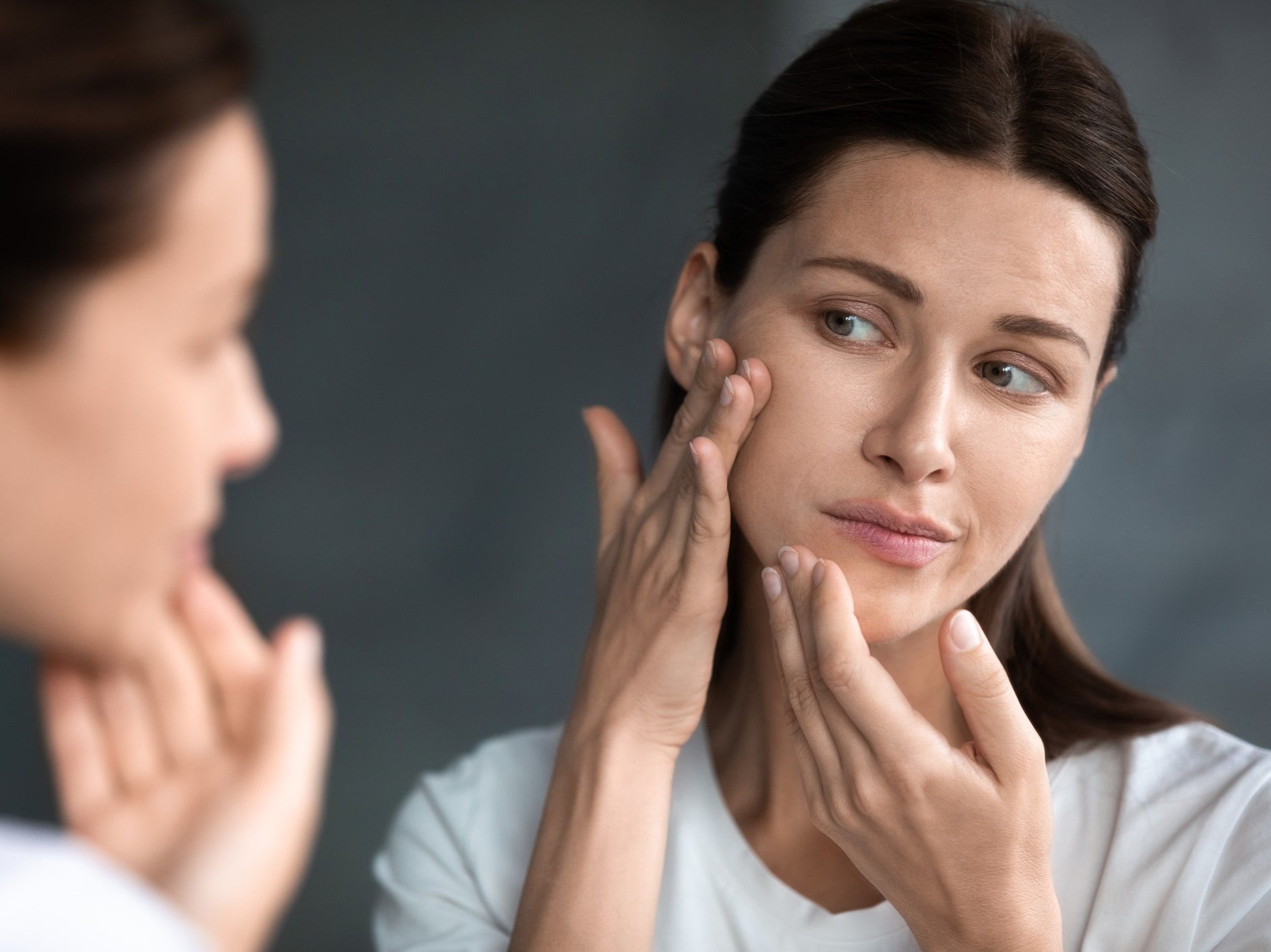 mulher analisando o próprio rosto no espelho