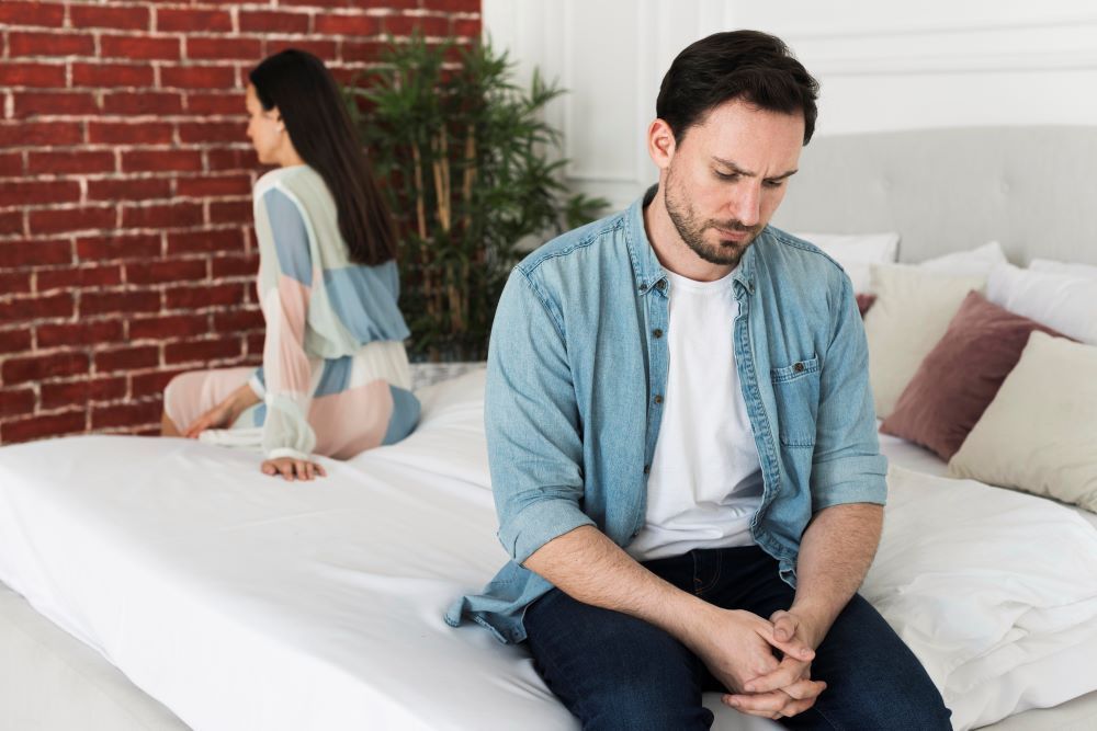 Homem sentado em uma cama de costas para uma mulher