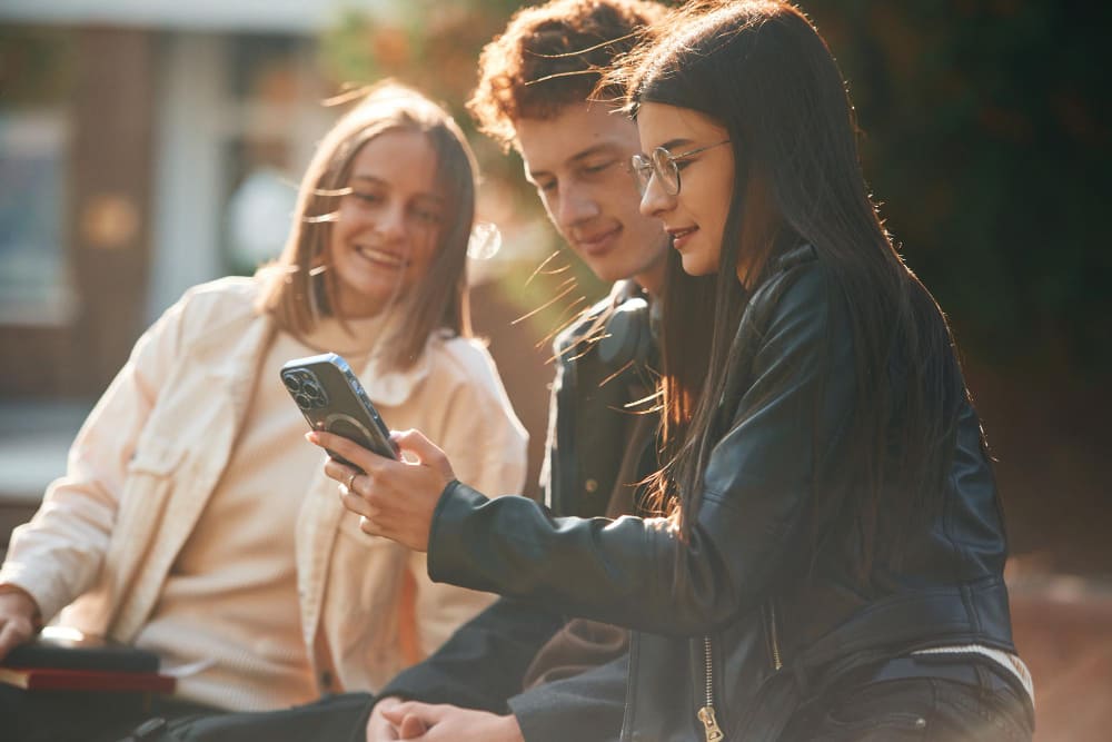 jovenes mirando móvil sentados exterior dos chicas un chico 
