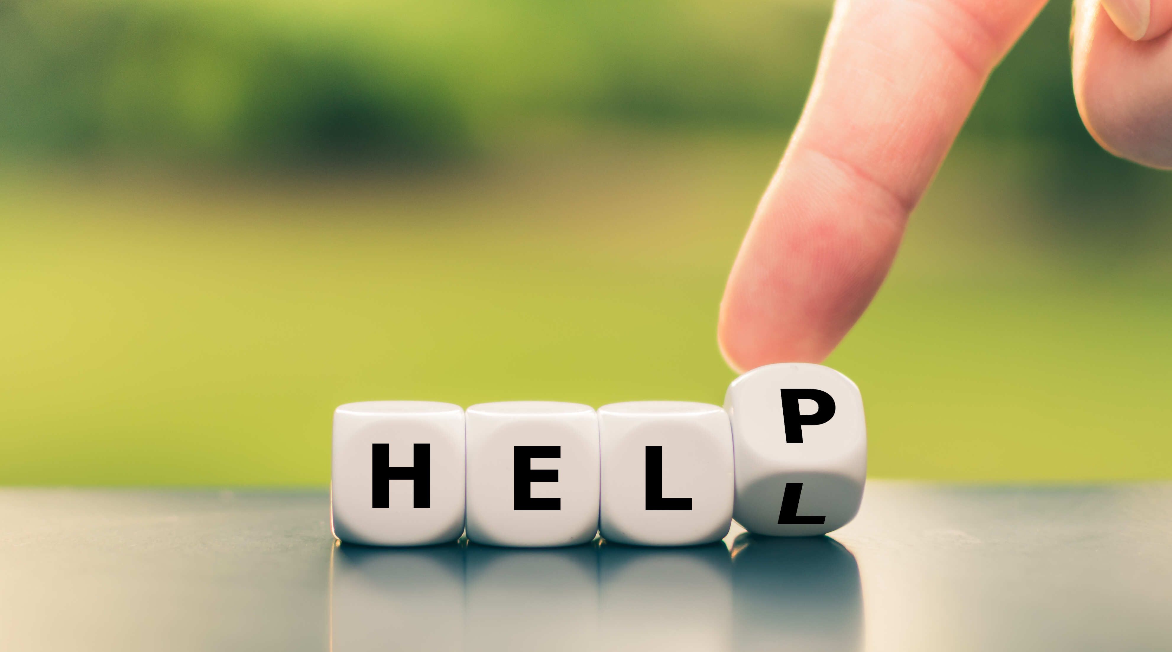 Zu sehen sind 4 Buchstabenwürfel und ein Zeigefinger, der den letzten Buchstaben von “L” zu “P” wechsel. Somit ergibt das Wort anstelle von “HELL” das Wort “HELP”.