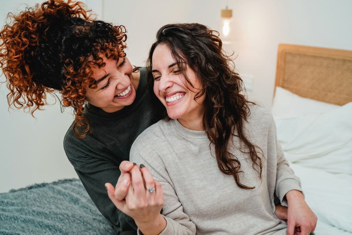dos chicas jóvenes sonriendo cogiéndose de la mano en la cama 