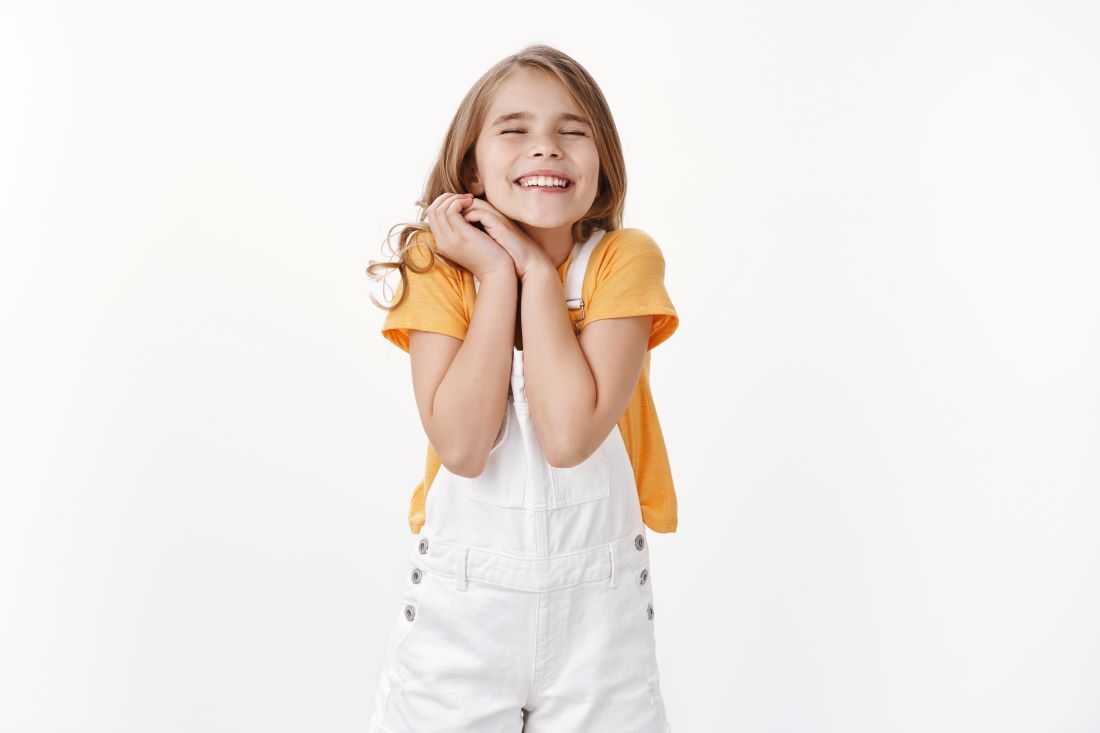 niña peto blanco camiseta amarilla sonriendo