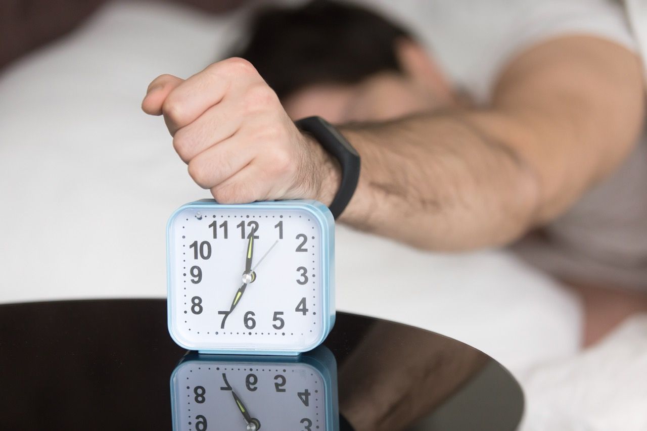 HOMBRE TUMBADO CAMA GOLPEANDO MANO RELOJ DESPERTADOR