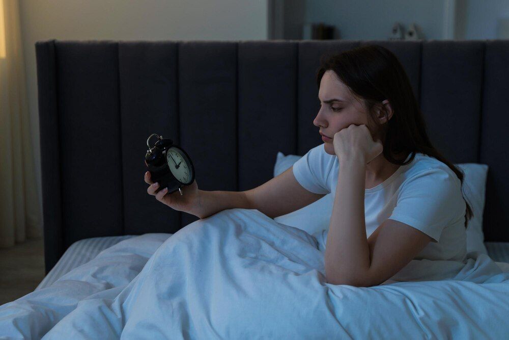 mujer joven frustrada con un despertador sufriendo de insomnio en la cama en interiores