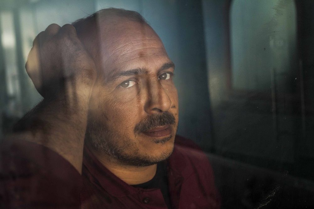 Foto eines Manns, der aus einer Fensterscheibe in die Ferne sieht.