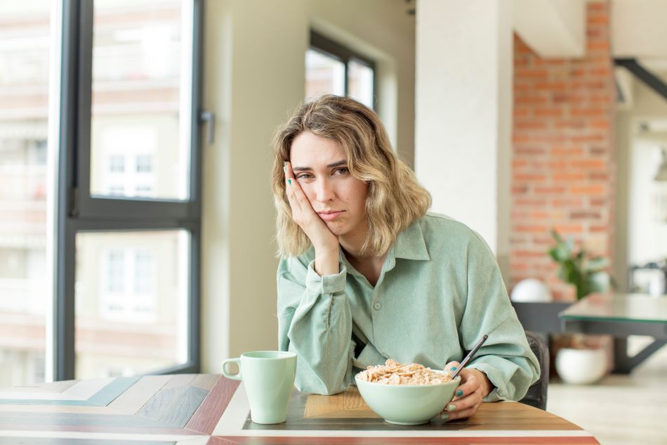 mujer camisa verde sentada mesa bol cereales miedo