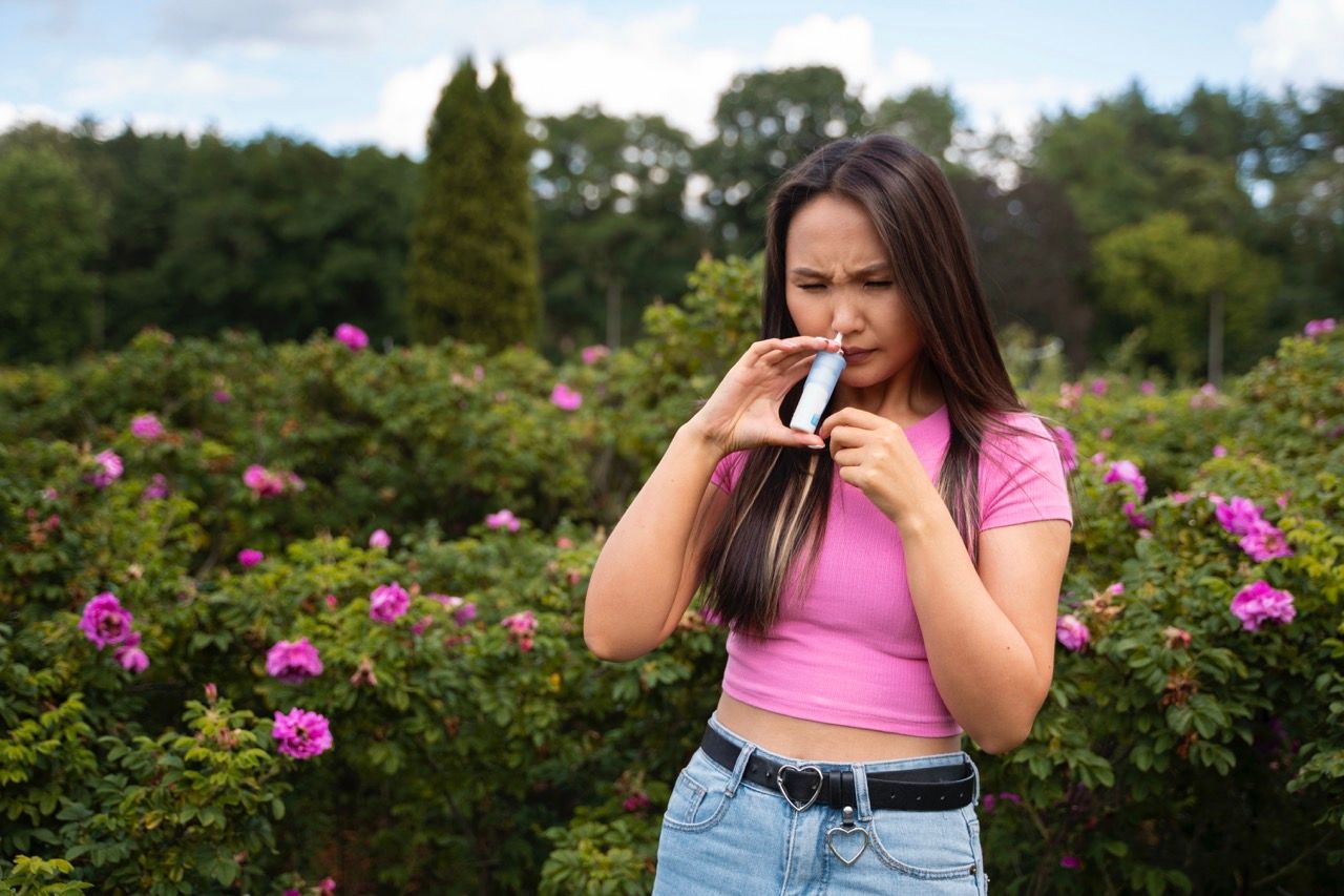 mujer morena pelo largo camiseta rosa usando spray nasal alergia 
