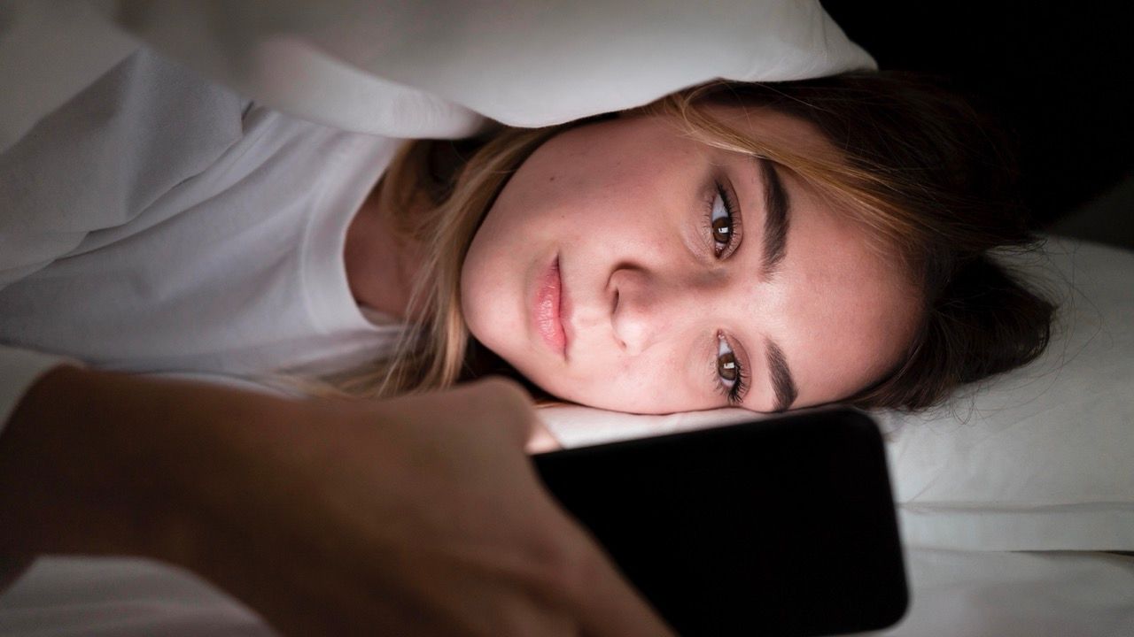 mujer tumbada cama mirando movil luz cara insomnio