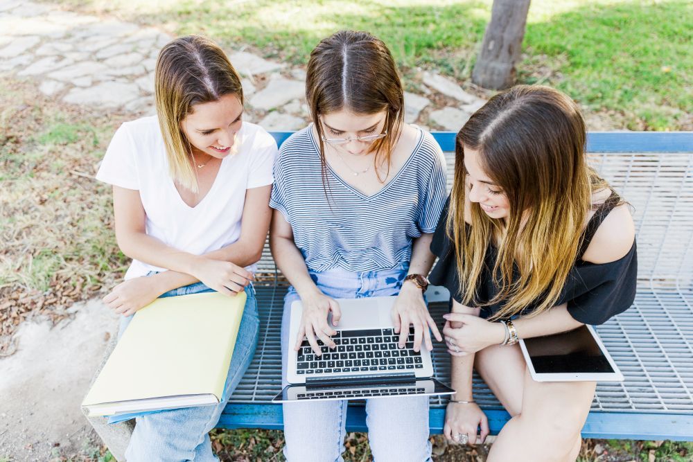 chicas jovenes sentadas banco aire libre mirando ordenador
