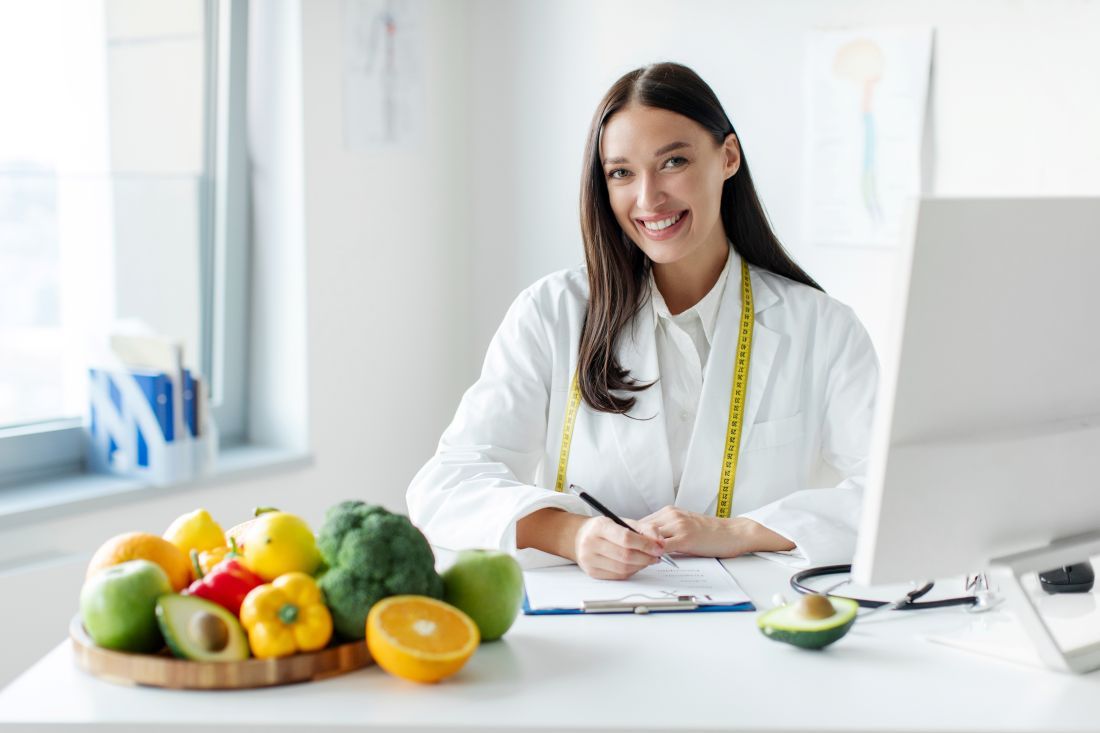 nutricionista mujer bata blanca metro sentada escribiendo fruta mesa