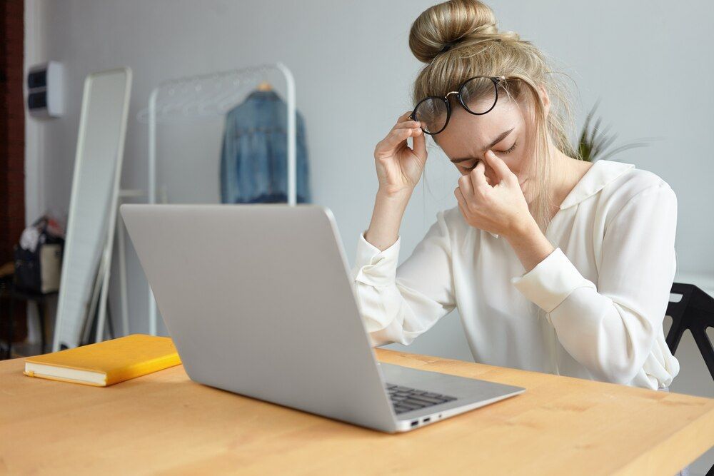 tecnologia moderna, conceito de trabalho e pessoas. retrato de uma jovem funcionária cansada com coque no cabelo tirando os óculos e massageando a ponte do nariz, sentindo-se estressada devido ao excesso de trabalho