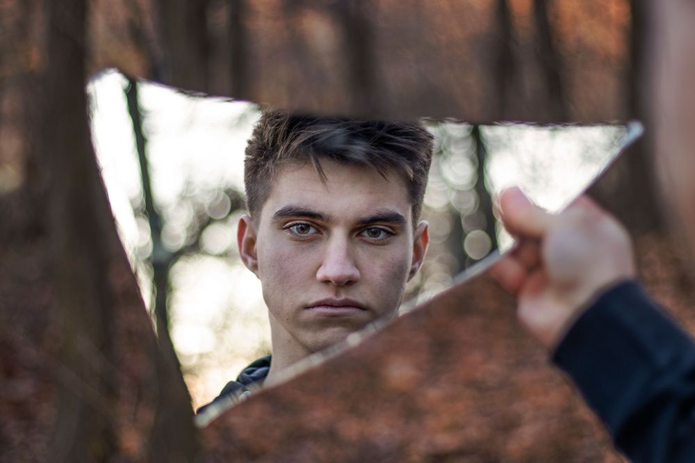 Foto eines Manns, der sein Gesicht in einer Spiegelscherbe beobachtet.