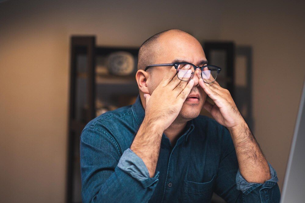 um jovem empresário trabalha no computador tarde da noite em uma sala mal iluminada ele está cansado e estressado precisa descansar tira os óculos e esfrega os olhos
