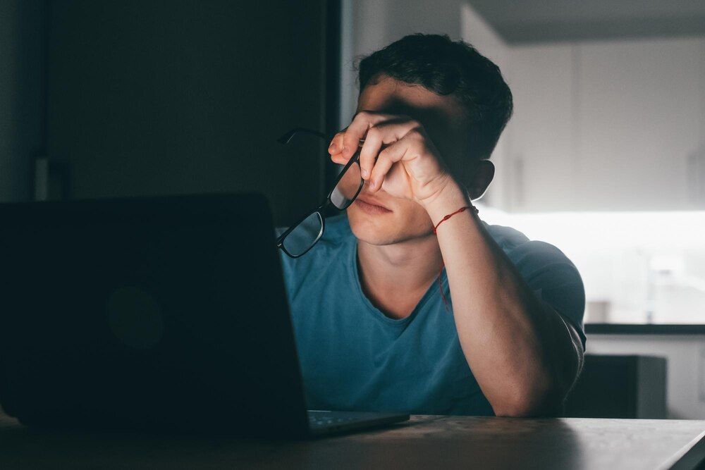 um homem jovem doente e cansado sentindo-se mal tocando seus olhos e rosto à noite após excesso de trabalho adolescente do sexo masculino com dor de cabeça trabalhando
