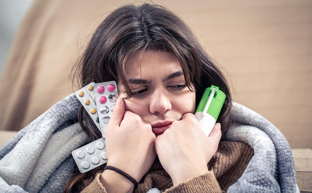 una joven enferma sosteniendo spray para la tos y pastillas en sus manos