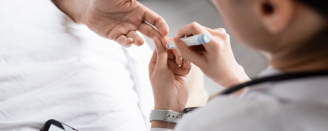 Immagine in primo piano di un medico che tiene in mano una penna pungidito vicino alla mano di un paziente diabetico in un reparto ospedaliero.