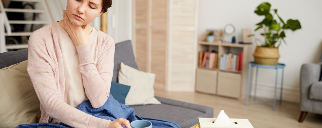 ragazza, seduta sul divano, si tocca la gola dolorante