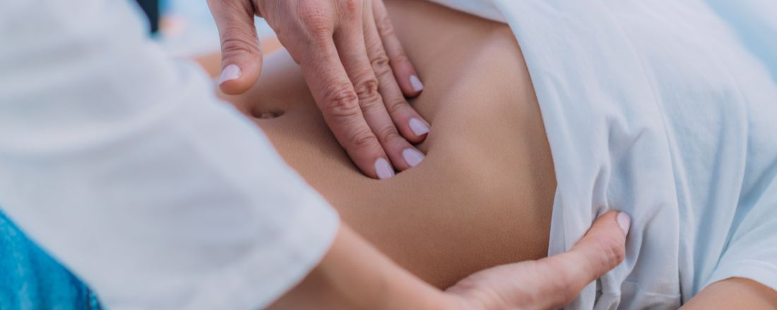 Primo piano di un medico che palpa l'addome di un paziente sdraiato.