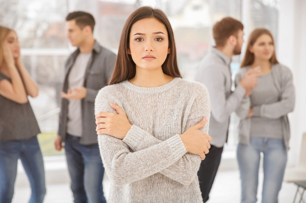 Ragazza che soffre di disturbo d'ansia sociale si stringe le mani al petto mentre si isola da un gruppo di persone che parlano e socializzano.