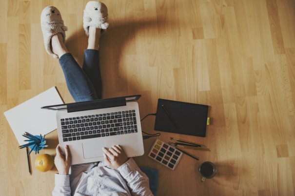 Persona seduta sul pavimento, in ciabatte e con il pc sulle gambe, che lavora da casa