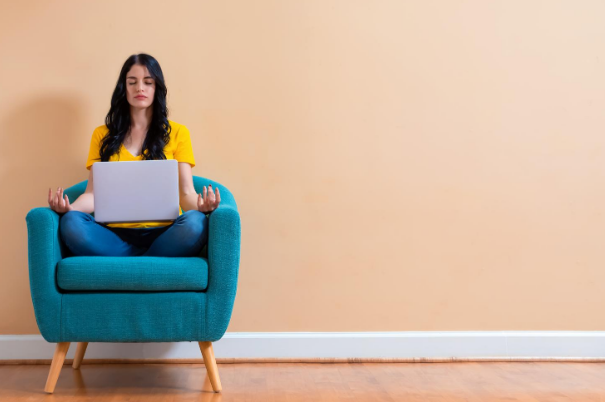 Donna seduta su una poltrona e con pc sulle ginocchia tenta di rilassarsi tramite una posizione yoga