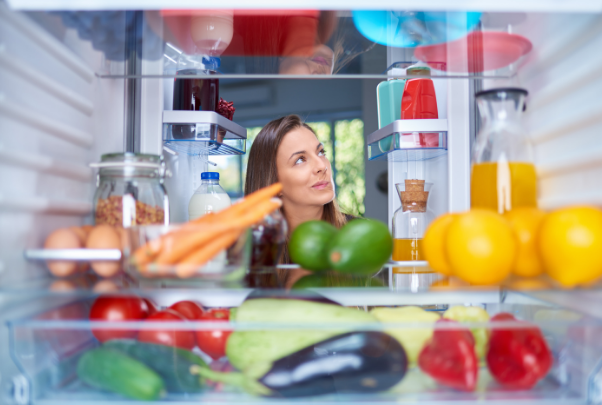 Donna osserva dubbiosa l'interno di un frigorifero pieno di alimenti colorati, per capire se li ha collocati nel posto giusto