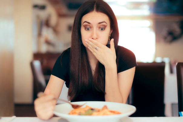 Una donna elegante si porta la mano alla bocca perché non si sente bene dopo aver ingerito un cibo al quale è allergica o intollerante