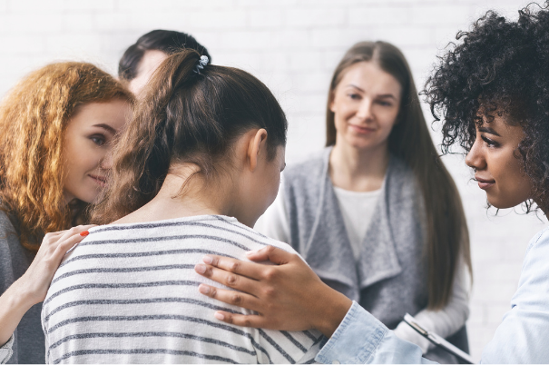 Un gruppo di ragazze di etnie e aspetto differente sono sedute in cerchio e si sostengono in una seduta di terapia di gruppo