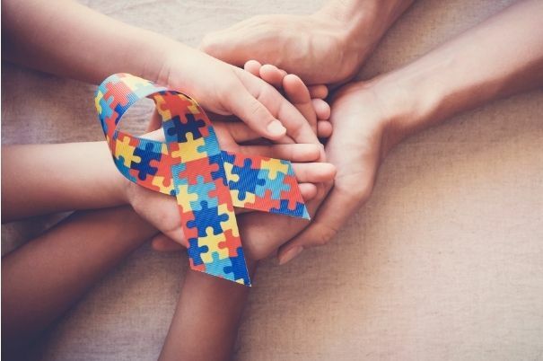 Fiocco con Puzzle Colorato Simbolo dell'Autismo Stretto in Mani di una Famiglia Caregiver di un Autistico
