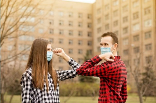 Giovane Coppia con Mascherina si Saluta con i Gomiti fuori di Casa senza Abbracci né Baci né Usando le Mani