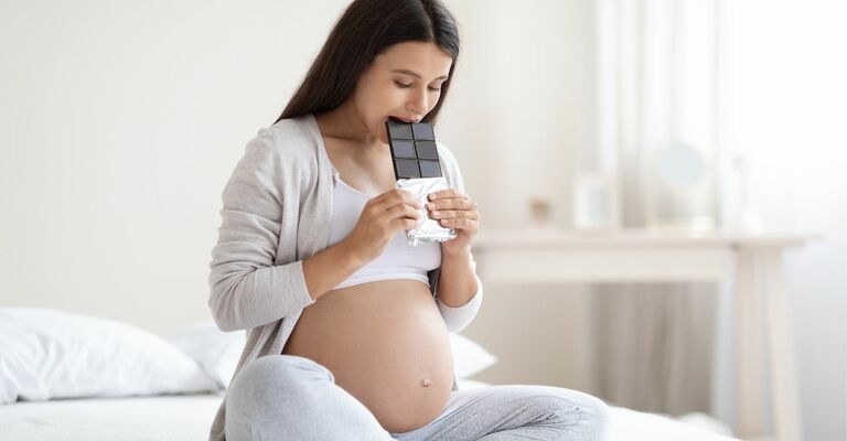 donna incinta seduta sul letto mangia cioccolato