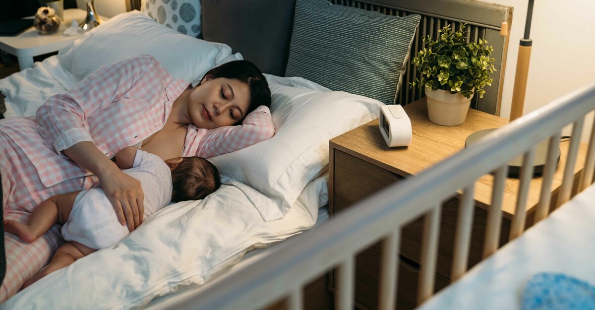 Donna a letto allatta il figlio sdraiata su un fianco