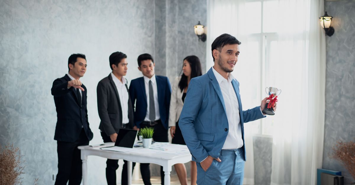 ragazzo al lavoro con una coppa in mano, colleghi parlano dietro alle spalle