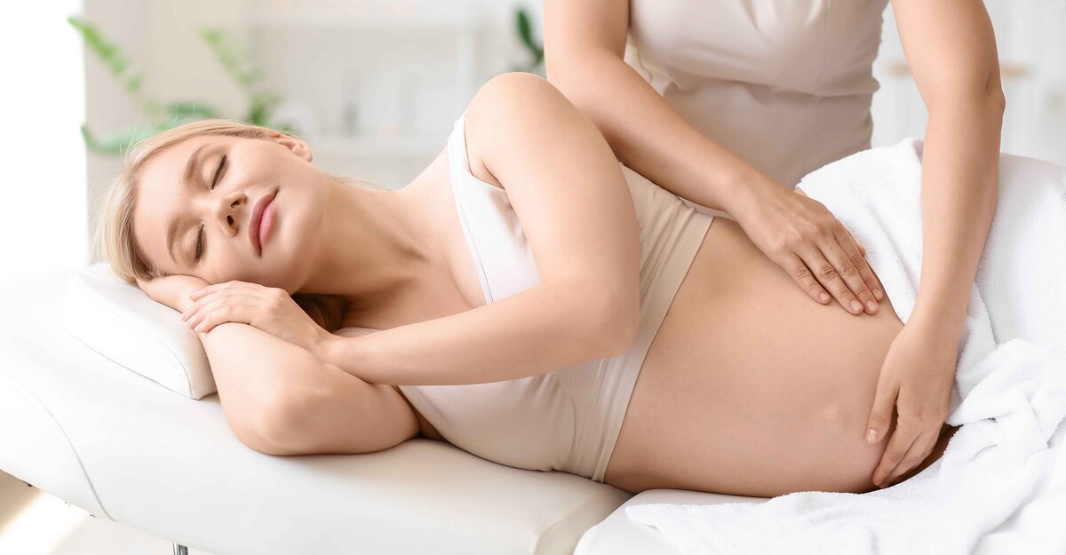 Donna in gravidanza si fa massaggiare la pancia stesa su un fianco