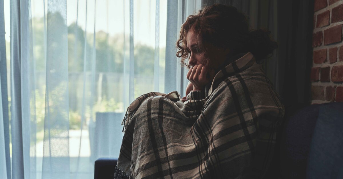 Ragazza in solitudine avvolta da una coperta alla finestra
